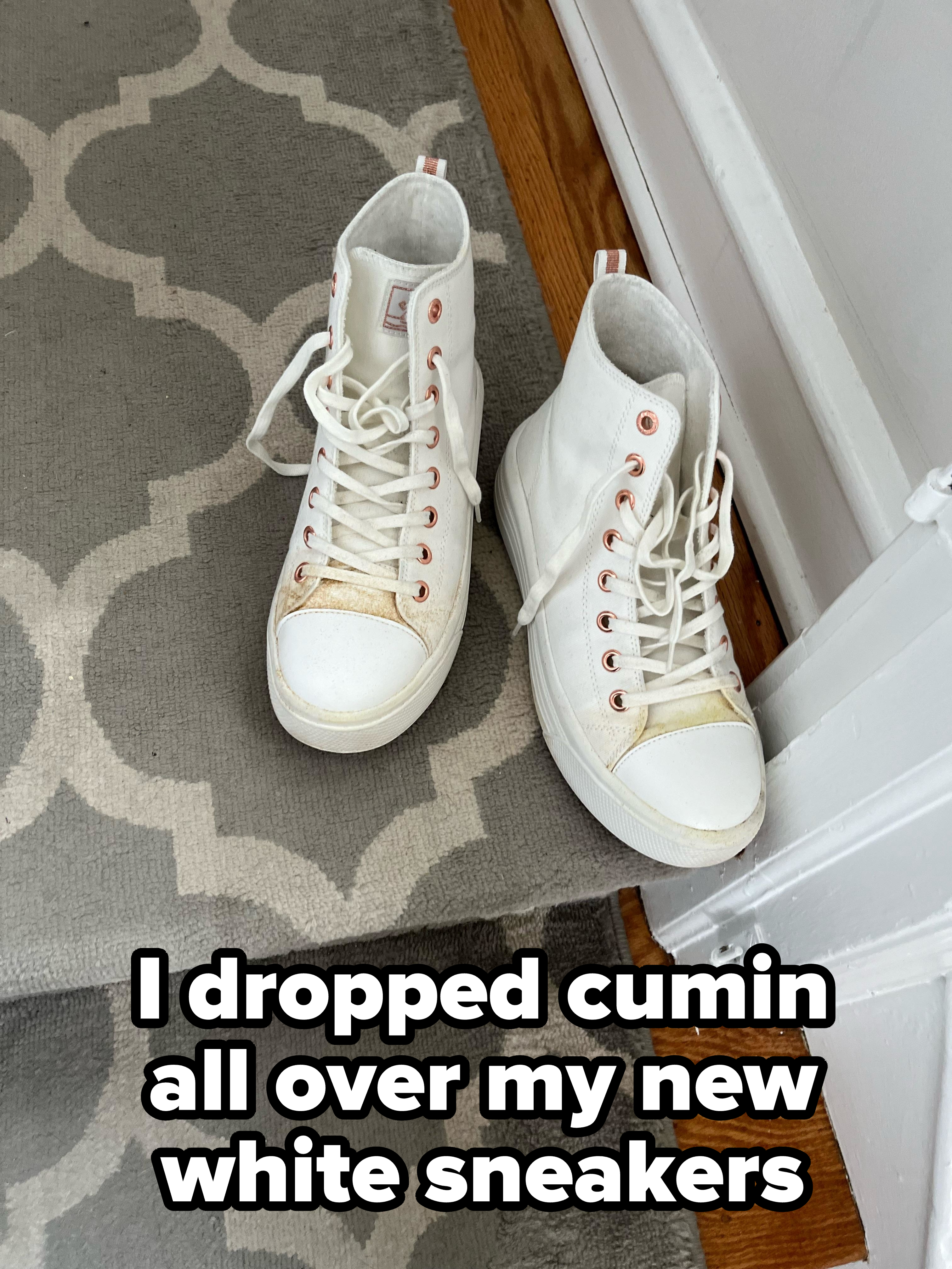 A pair of white high-top sneakers with lots of reddish stains are on a patterned floor next to a door