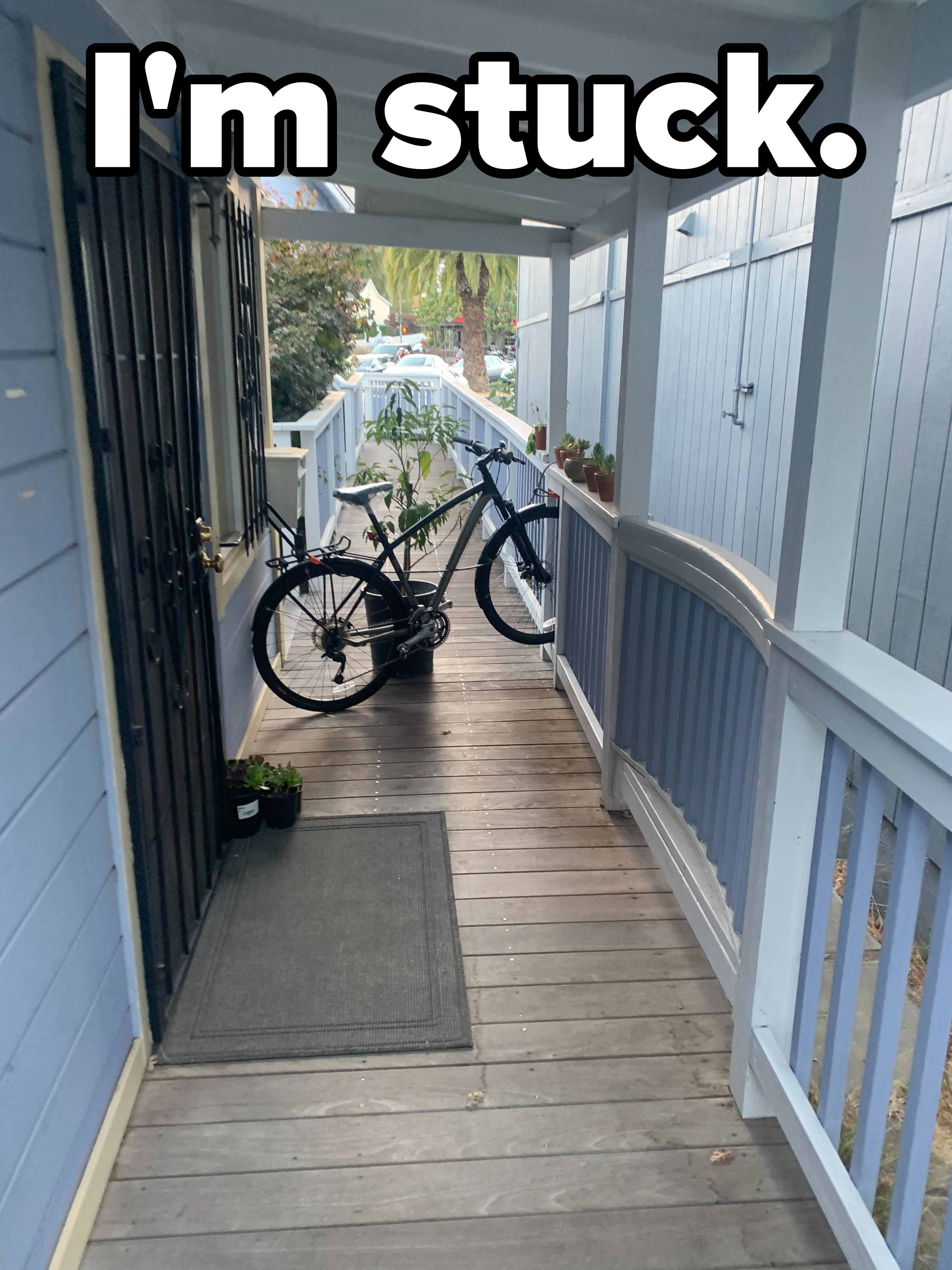 A bicycle is stuck sideways between a fence and a wooden railing on a long, narrow porch