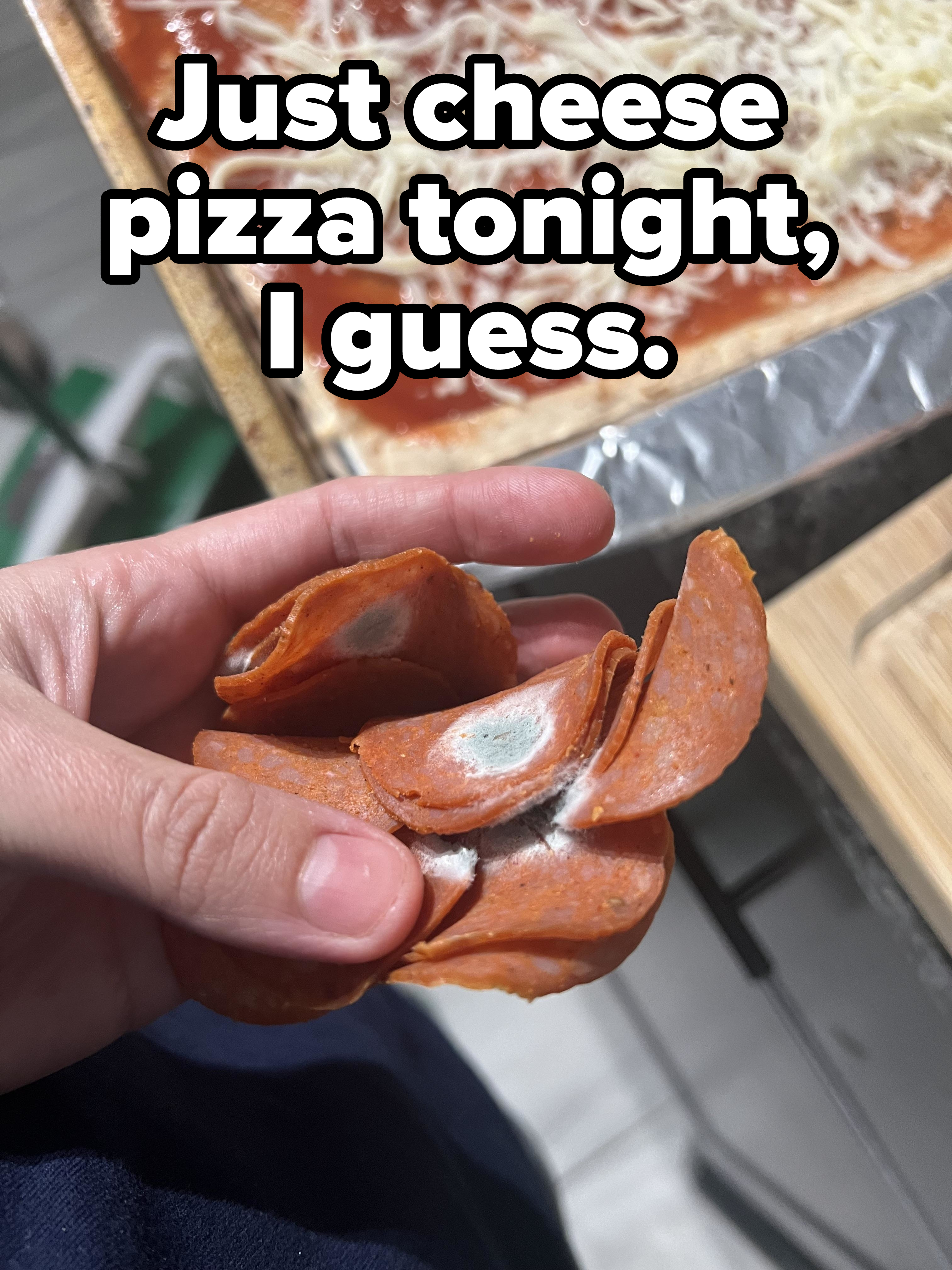 Hand holding slices of pepperoni with visible mold above a pizza pie