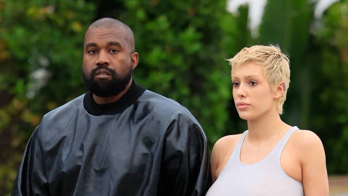 Kanye West and a woman walking together; Kanye in a black outfit, the woman in a gray tank top