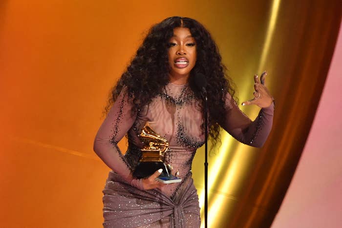 SZA on stage holding her Grammy award, wearing an embellished sheer gown