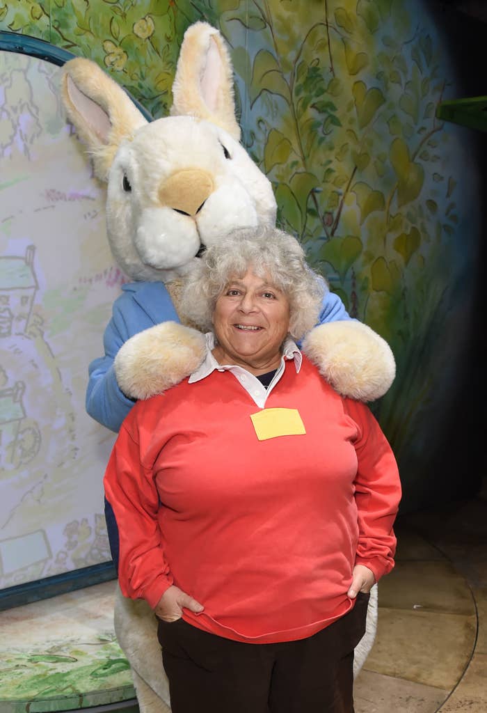 Person posing with a large costumed character resembling a rabbit, standing in front of an illustrated backdrop