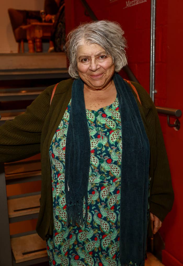 Woman in patterned dress and cardigan with scarf smiling indoors