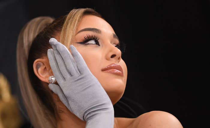Ariana Grande wearing sleek ponytail and satin gloves, touching her face, looking away