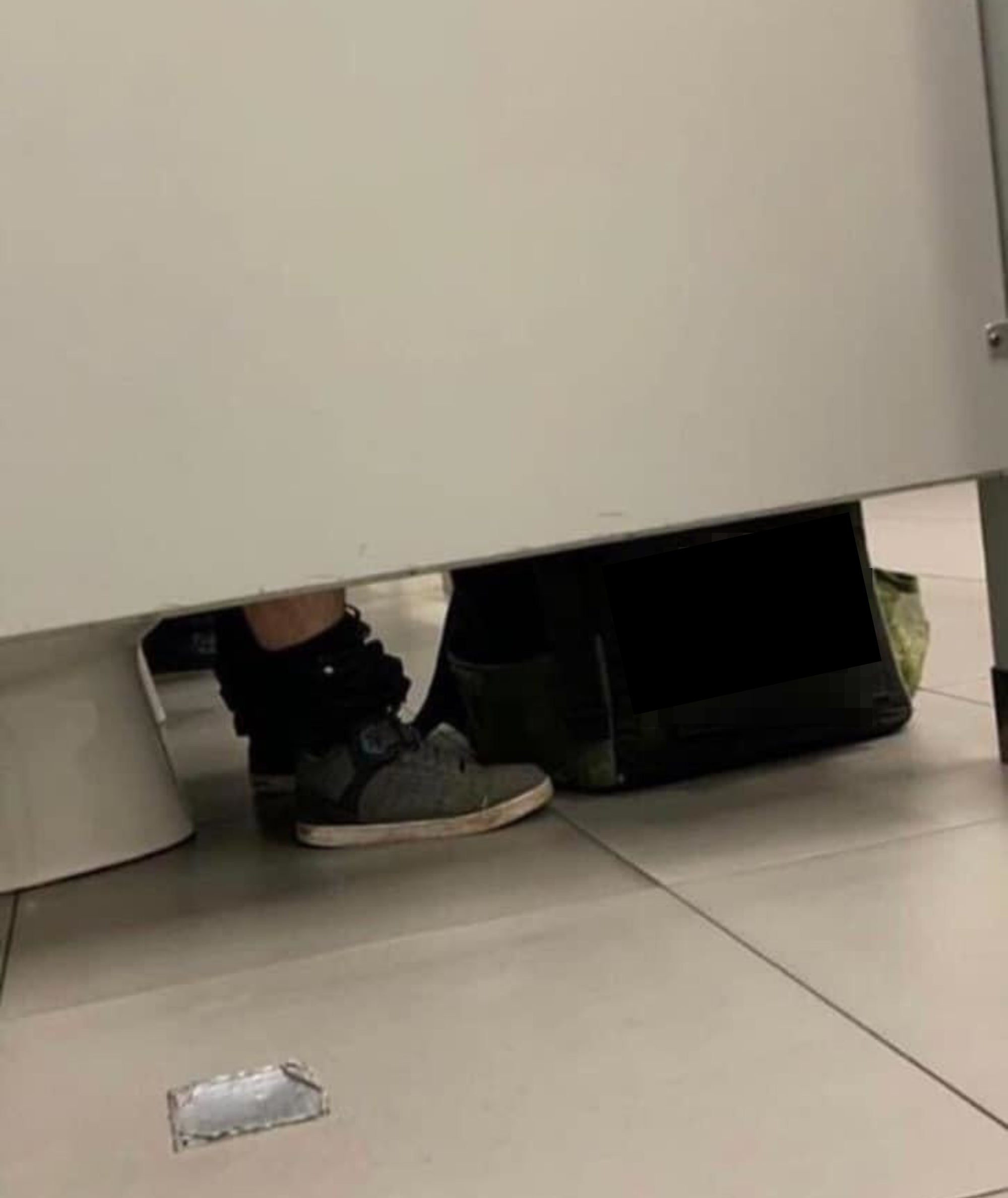 Person sitting in a public restroom stall with an Uber Eats bag visible on the floor under the door