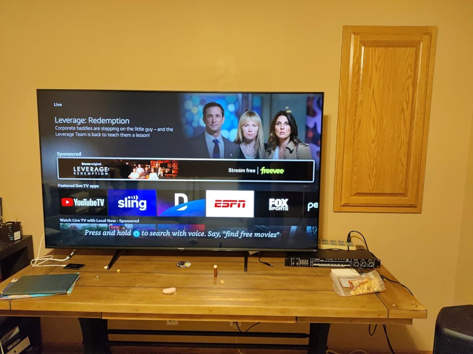 Smart TV displaying &#x27;Leverage: Redemption&#x27; ad on a user interface, with remote on table in a living room setting
