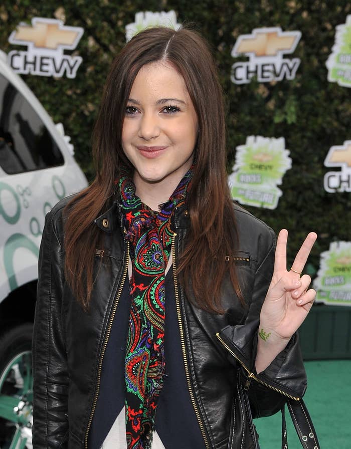 A younger Alexa wearing a patterned scarf and leather jacket, posing with a peace sign