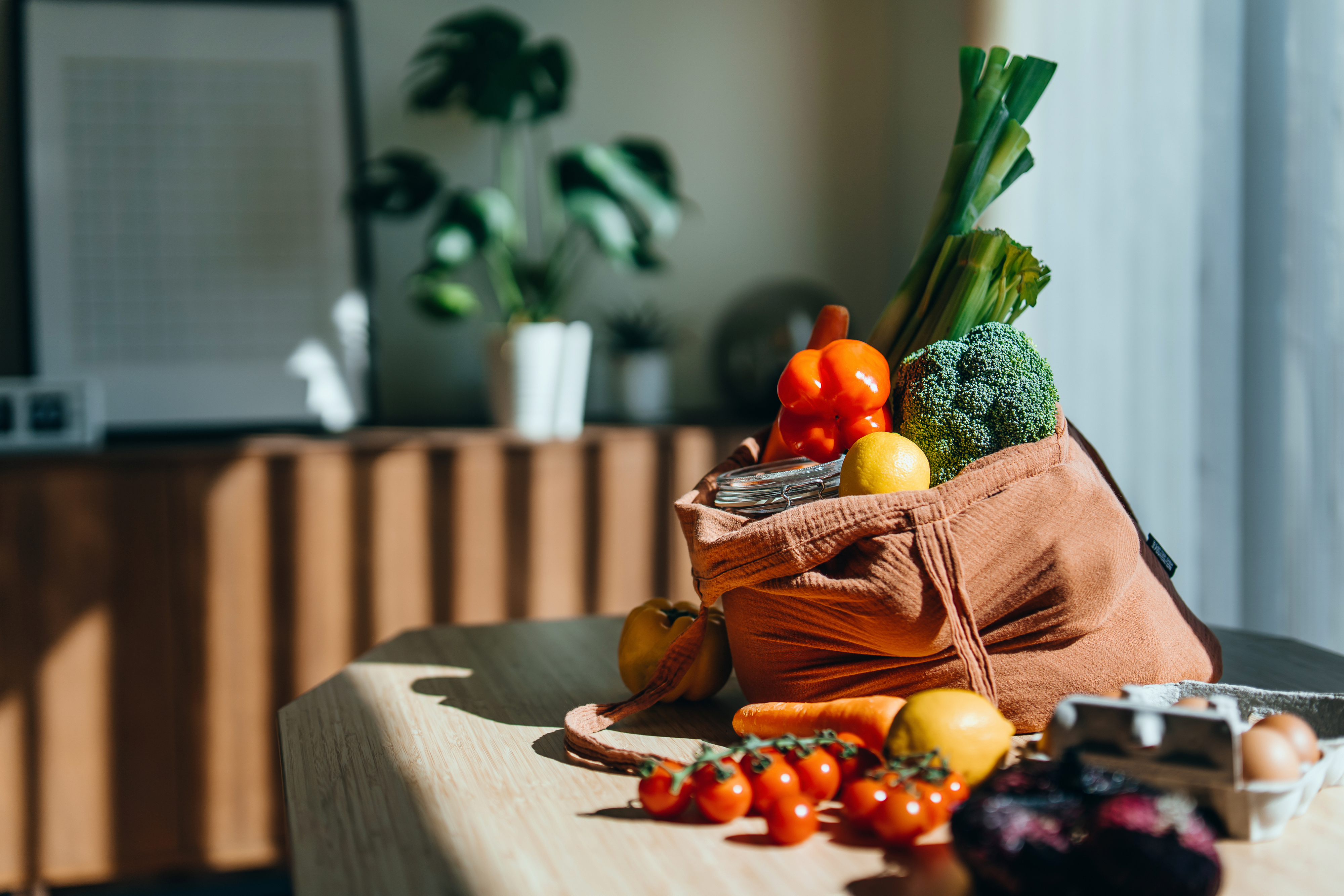 Groceries in a reusable bag on a table, suggesting preparation for a healthy home-cooked meal