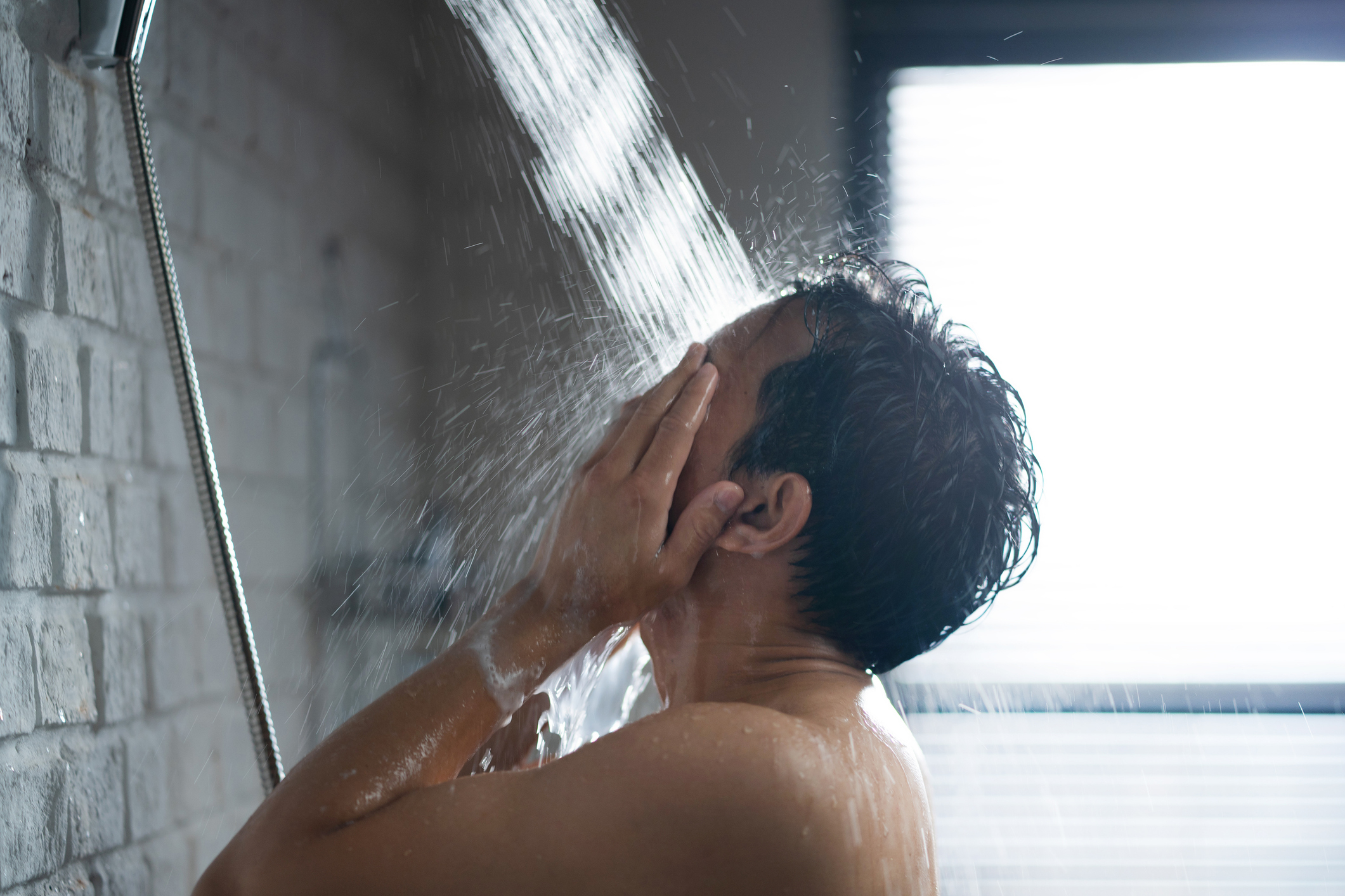 Person showering, facing away, with water flowing over them