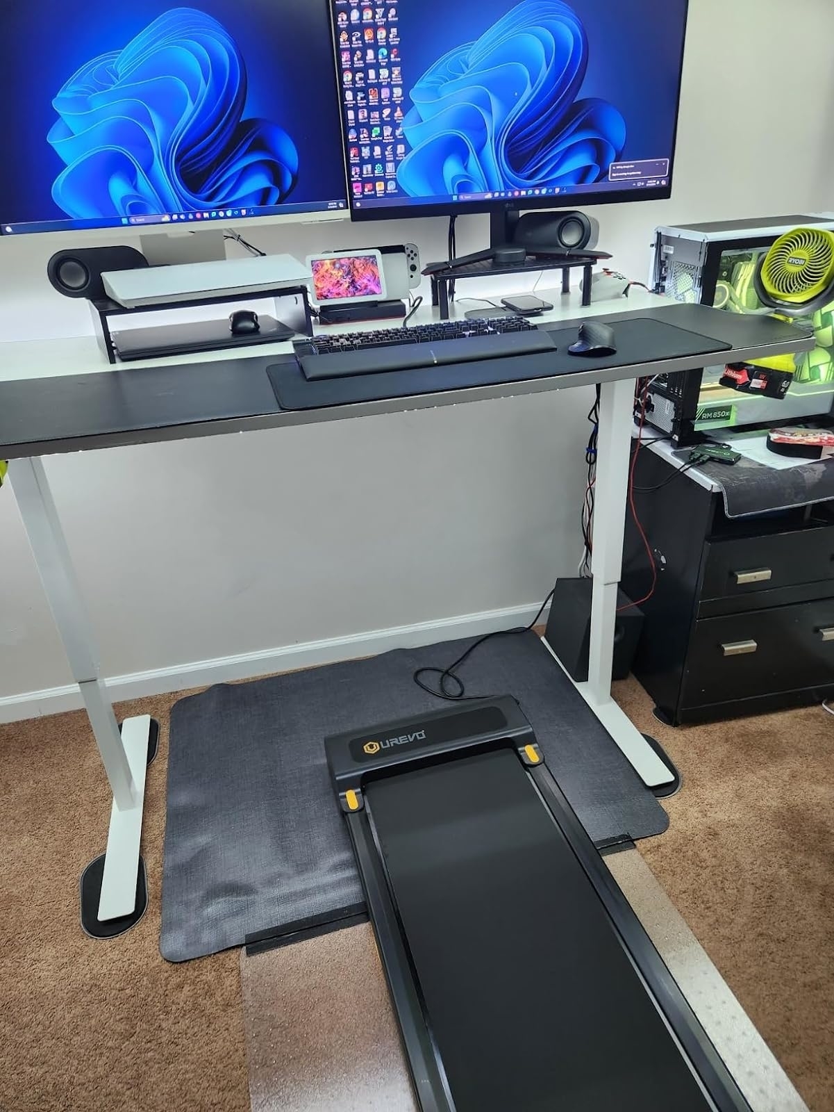 Home office setup with a standing desk, dual monitors, and treadmill set up underneath