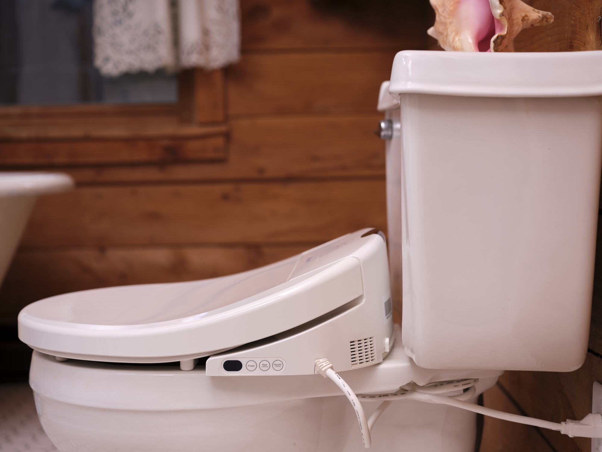 Bidet toilet seat with control panel, attached to a white toilet in a wooden-themed bathroom