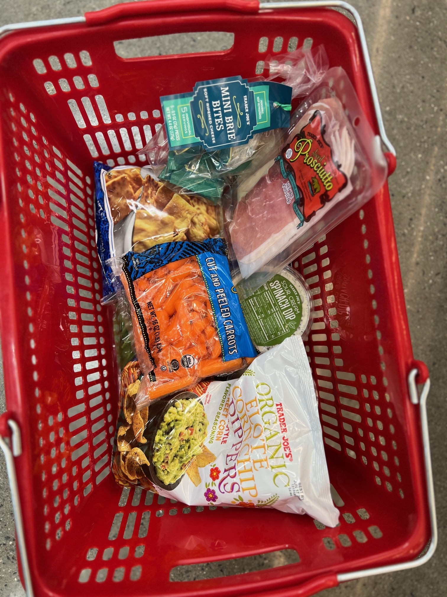 Shopping basket filled with various food items, including chips, salad mix, and packaged meat