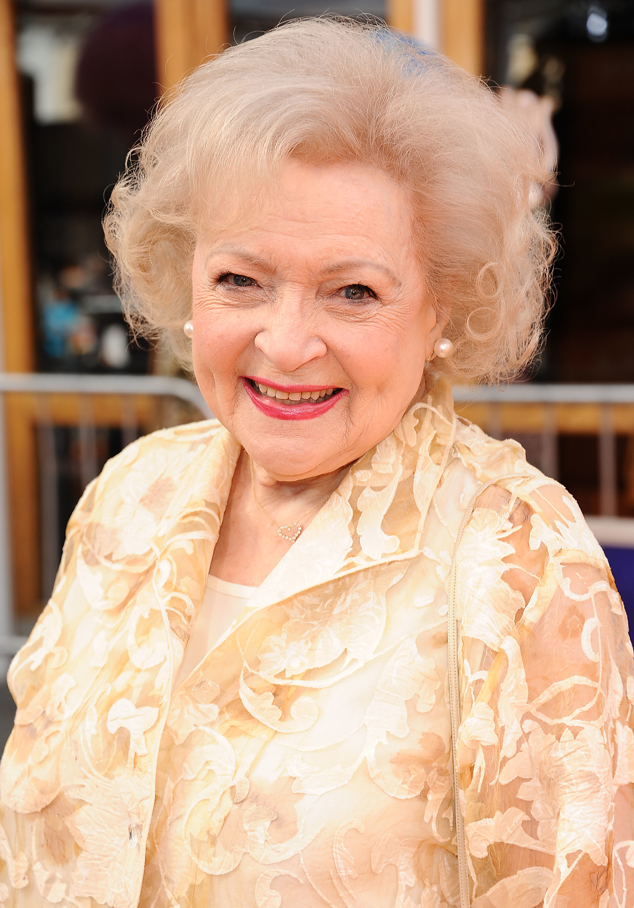 Betty White smiling, wearing a floral-patterned jacket with pearl earrings at an event
