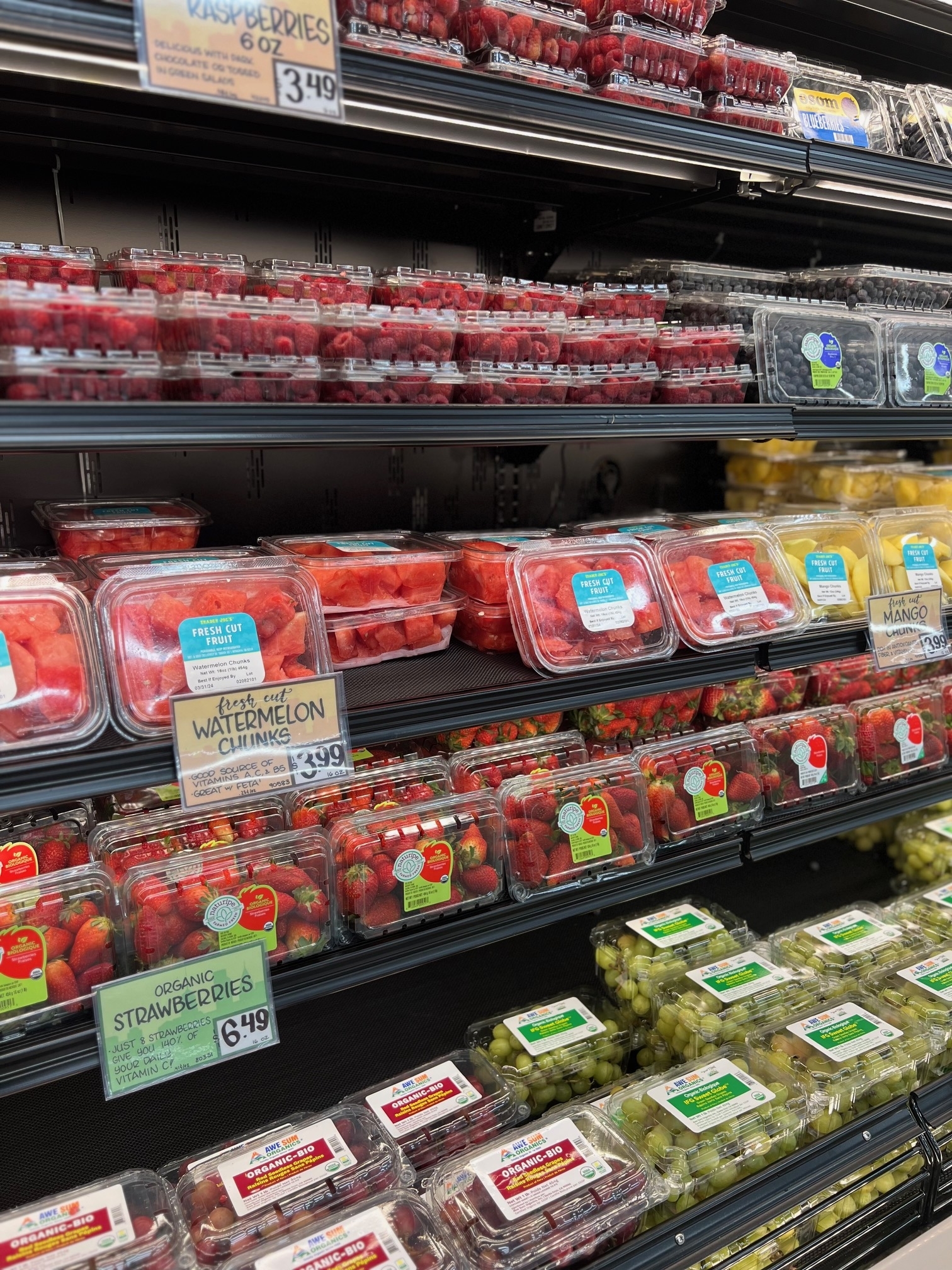 Refrigerated grocery store shelf stocked with various pre-packaged fresh fruit containers, including watermelon, strawberries, and grapes
