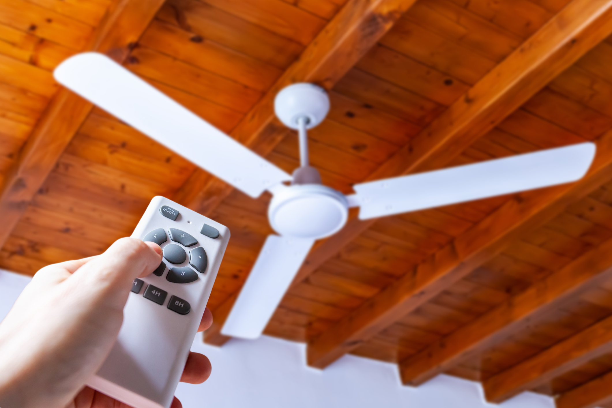 Person holding a remote to control a ceiling fan with wooden beams overhead