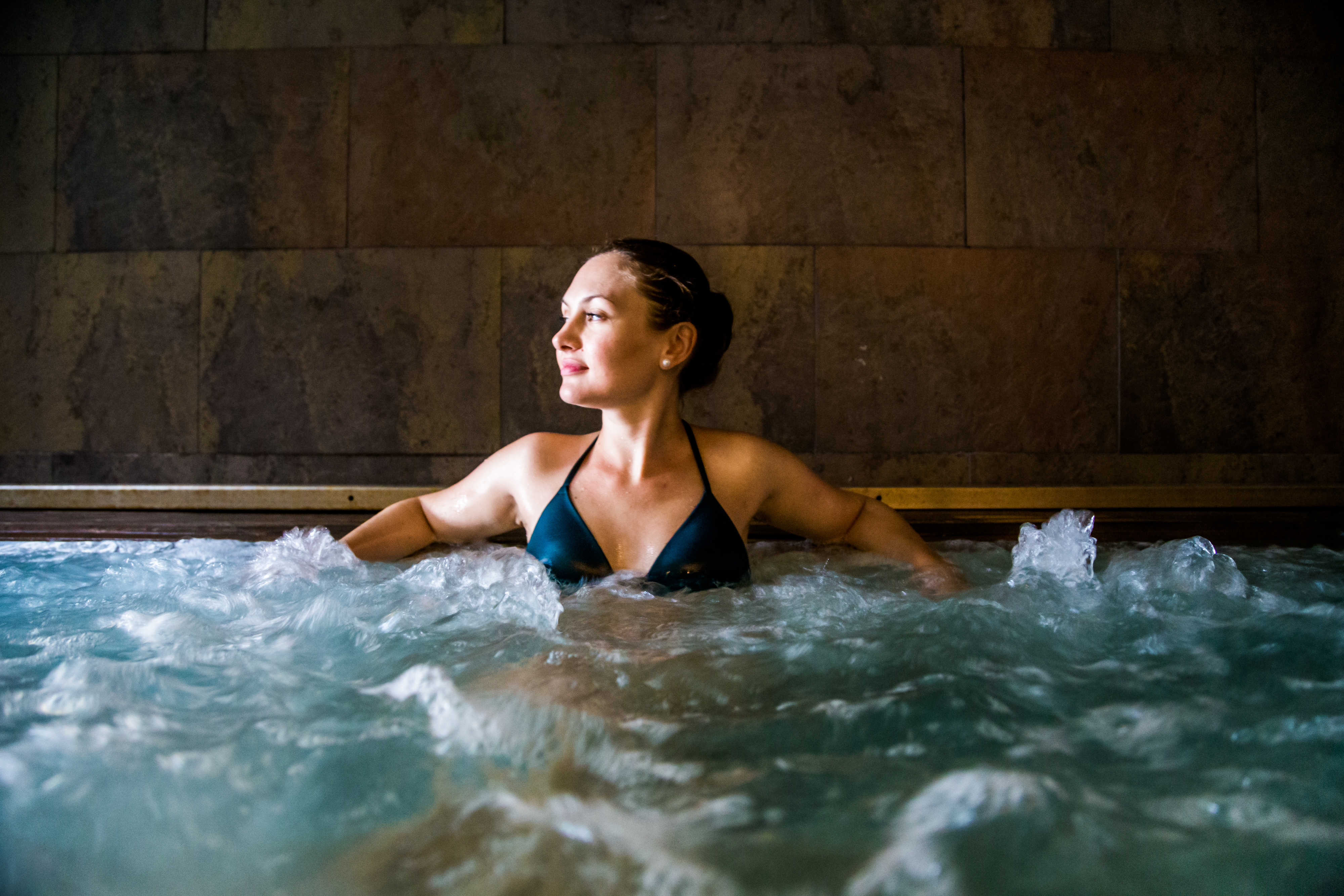 Person in a swimwear relaxing in bubbling water, gazing away thoughtfully