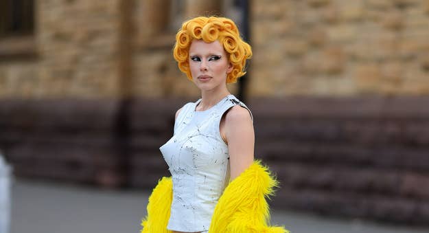 Woman in avant-garde white dress with yellow feather details, sporting sculptural orange hair