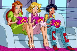 Sam, Clover, and Alex from "Totally Spies!" animated show sitting on a couch, each holding a flower-shaped pillow