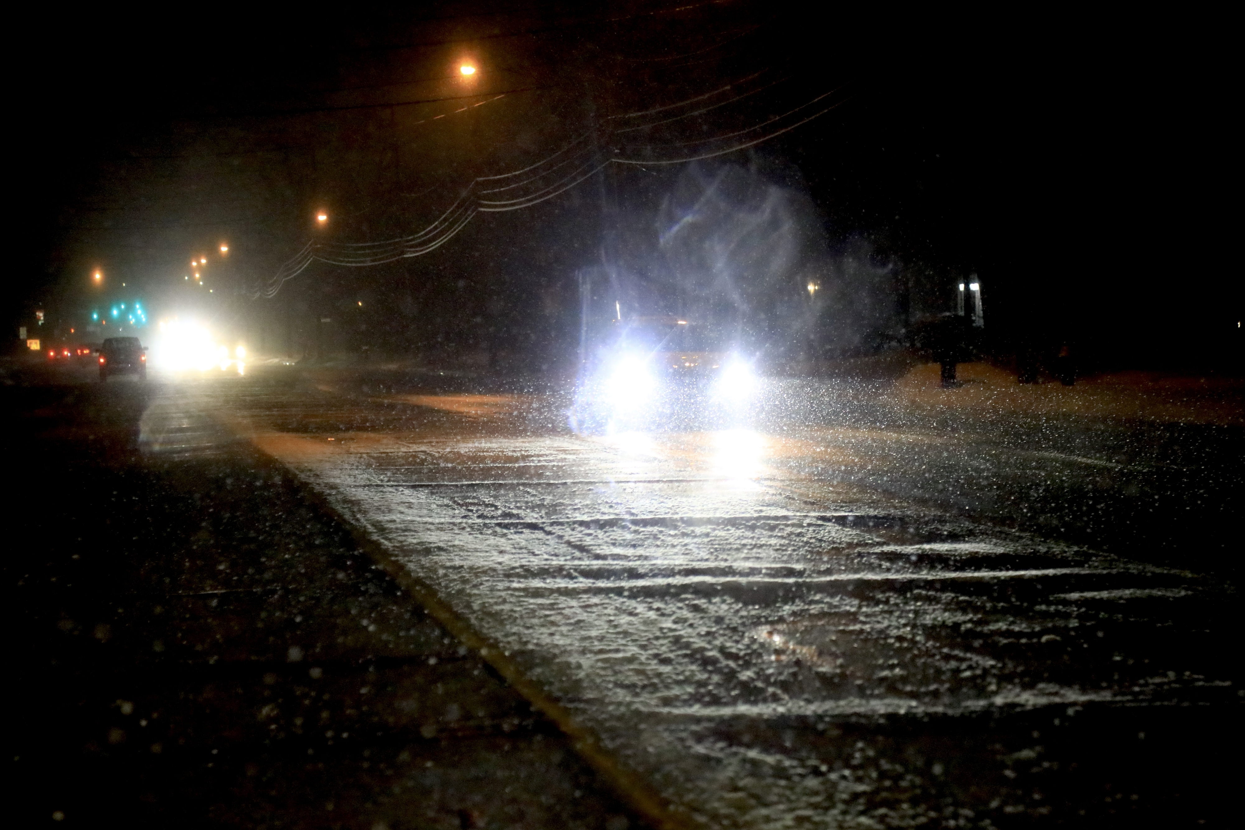 Car headlights illuminate a wet road at night with visible rain