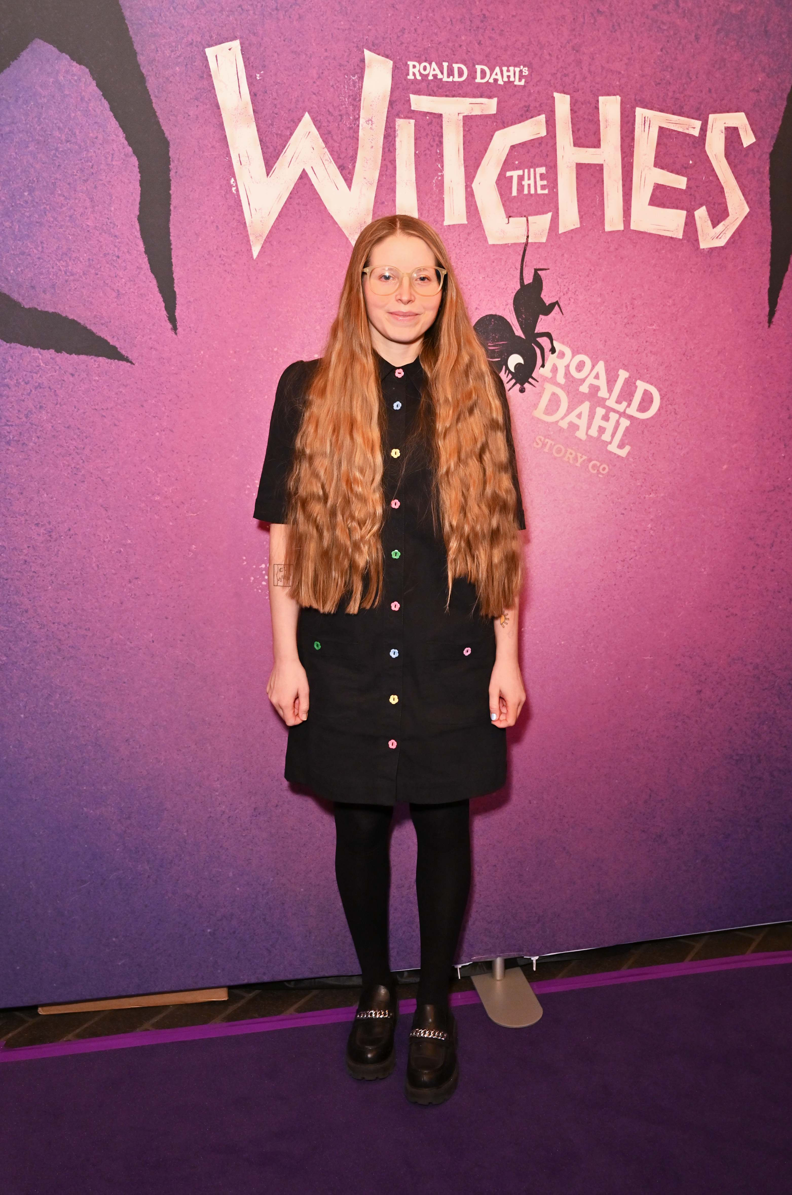 Jessie stands before &#x27;The Witches&#x27; backdrop wearing a dress and platform shoes at a premiere