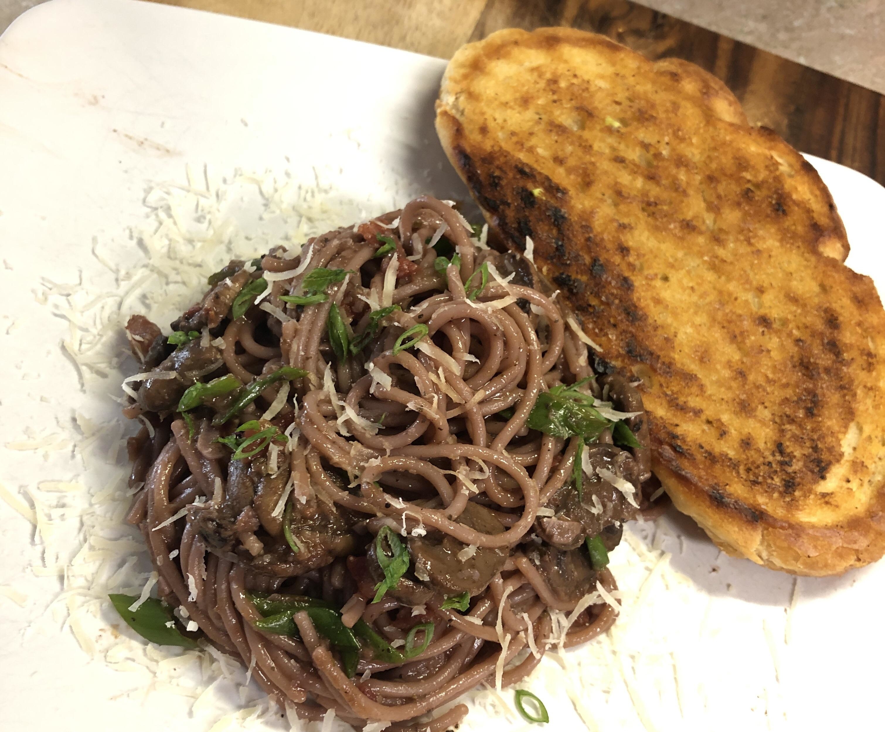 Plate of spaghetti cooked in red wine with herbs and a slice of garlic bread on the side