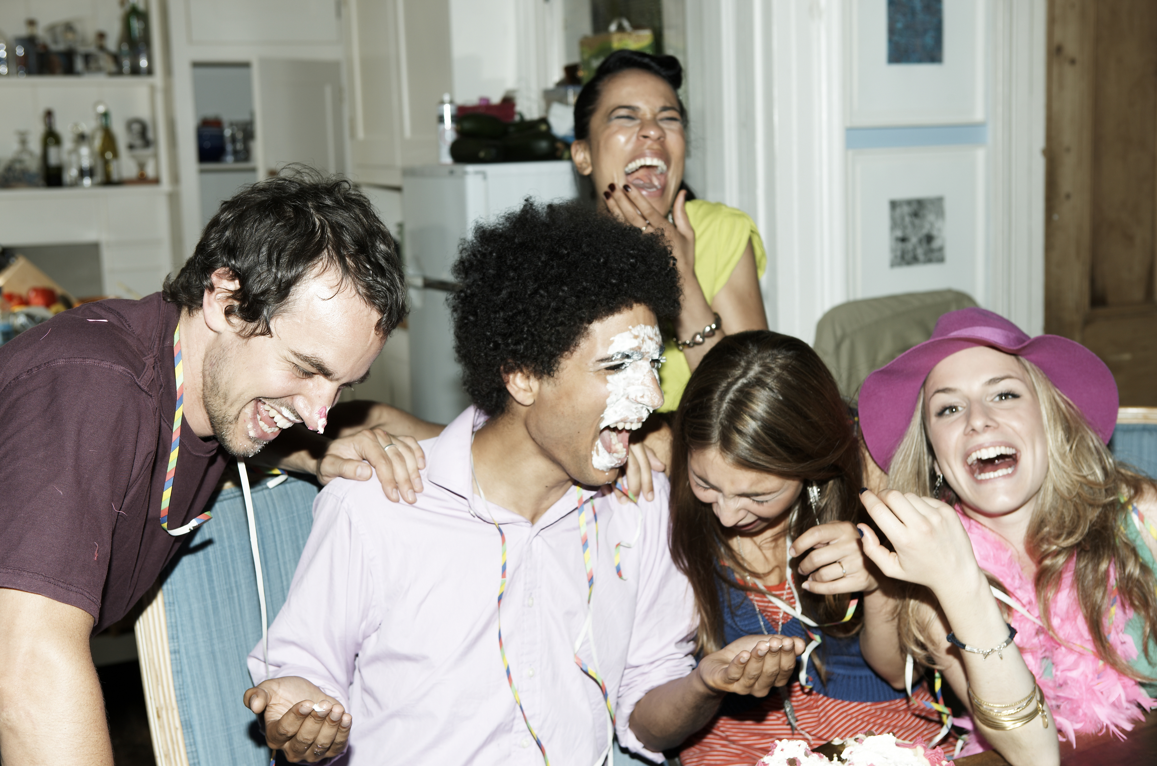 A group of people laughing together at a party, one with a face covered in cake