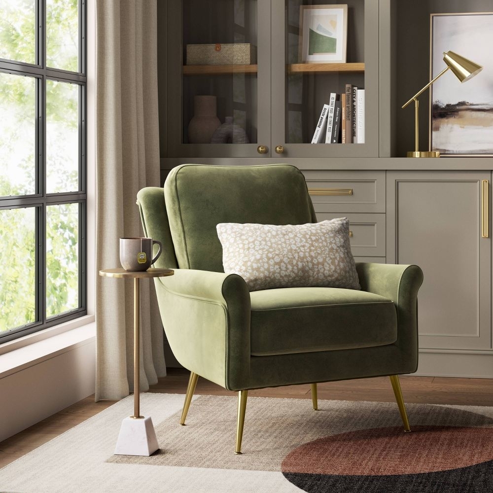A green velvet armchair with a white pillow in a stylish room setting