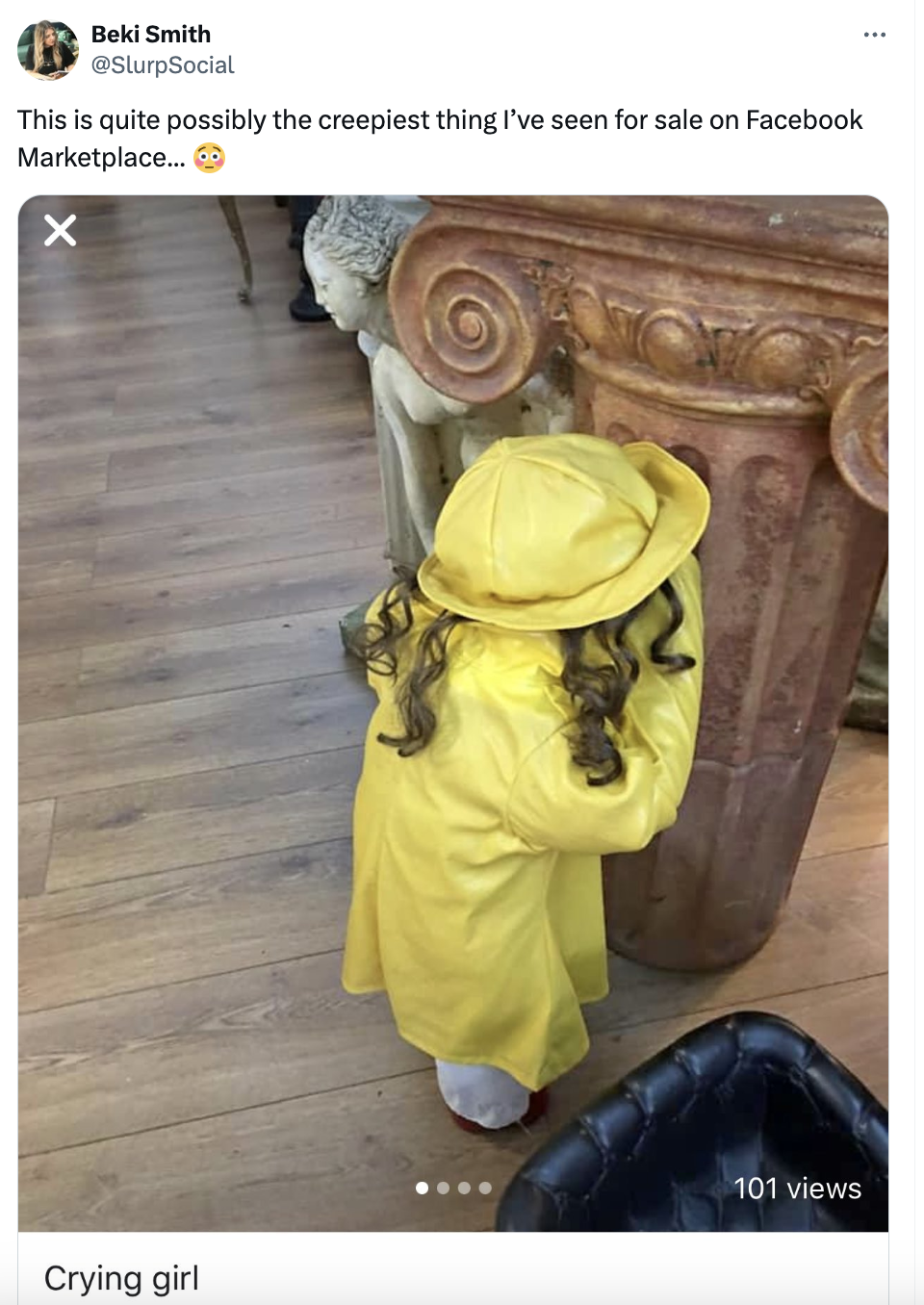 Child-sized mannequin in yellow raincoat and hat, facing a corner, in a room with furniture