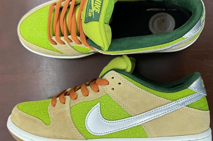Nike sneakers with green highlights and orange laces on a wooden surface