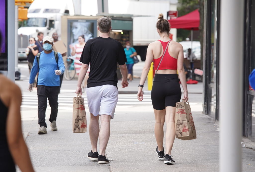 Two people walking away on a city street carrying grocery bags, suggesting a lifestyle element related to food