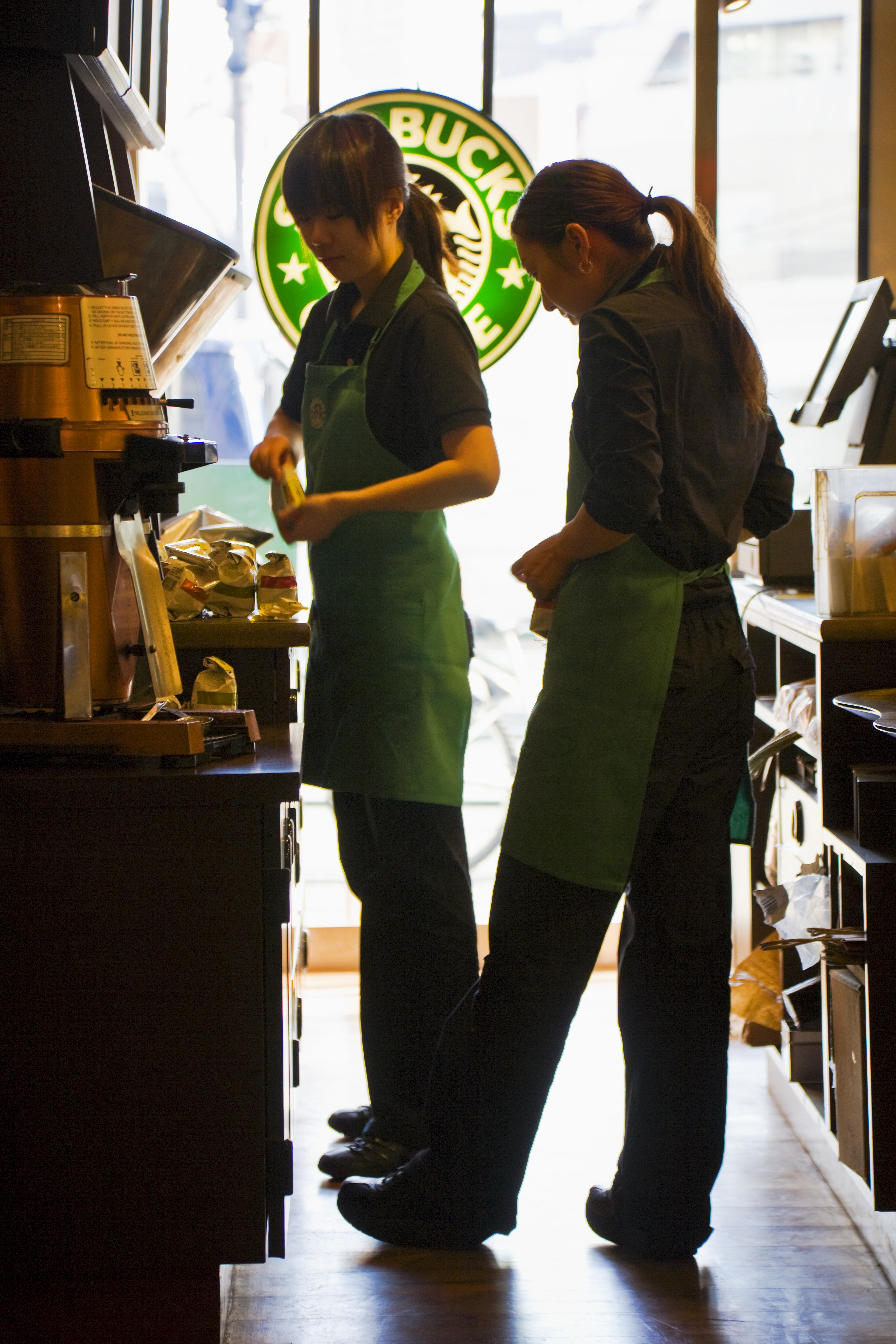 Two baristas in green aprons working behind the counter at a Starbucks store