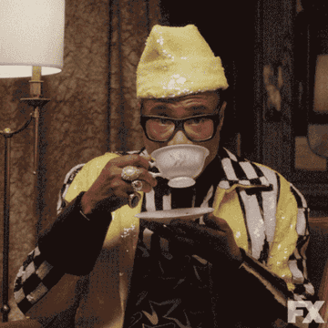 Person in a yellow hat and black-and-white outfit sipping from a teacup