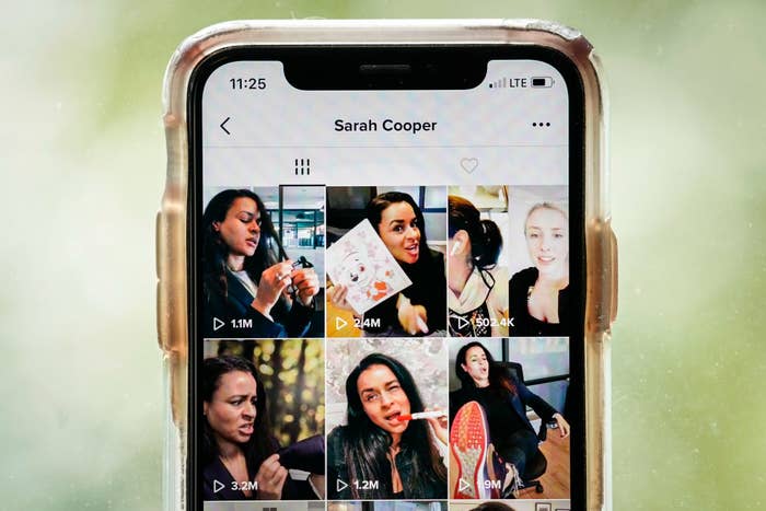 Hand holding a smartphone displaying a social media profile named Sarah Cooper with various video thumbnails