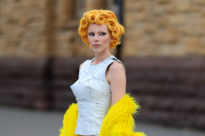 Woman in avant-garde white dress with yellow feather details, sporting sculptural orange hair