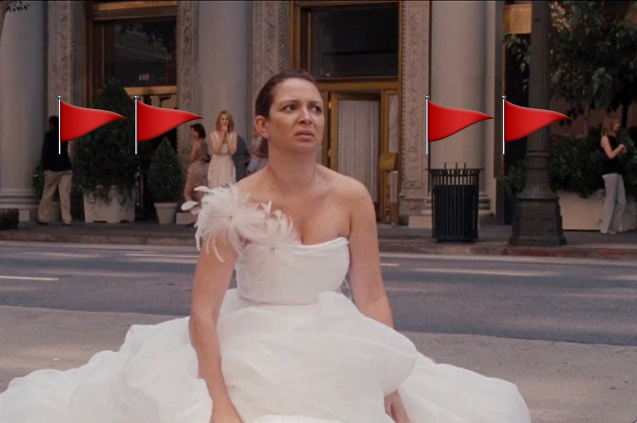 A woman in a white wedding dress sits on street, looking up, with bystanders in background