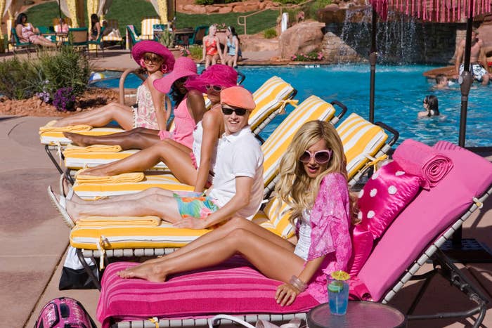 Three people lounging on poolside chairs, smiling at the camera, with towels and a water feature behind them