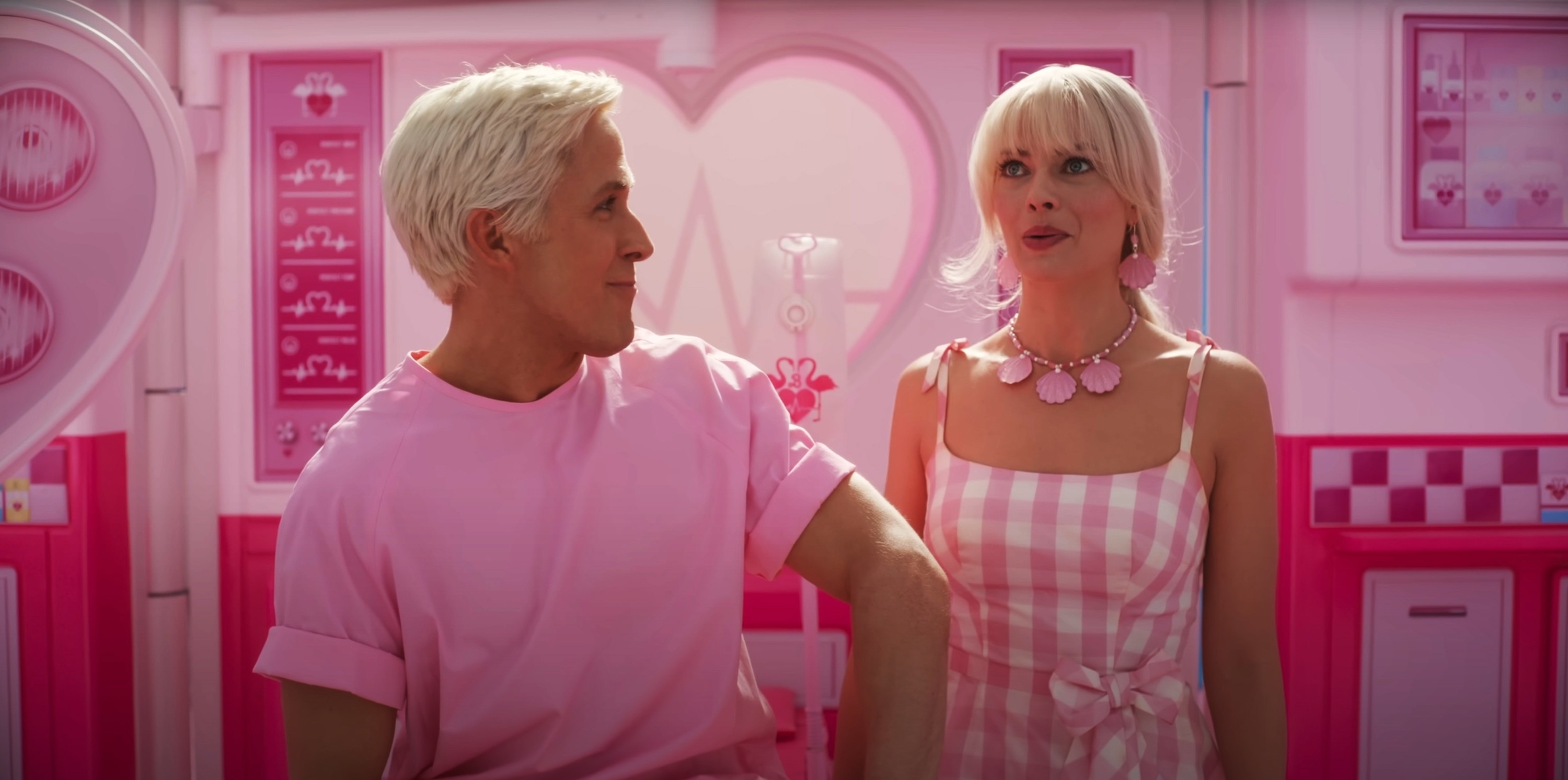 Two actors in a pink-themed scene, male in a plain t-shirt, female in a checkered dress with statement necklace