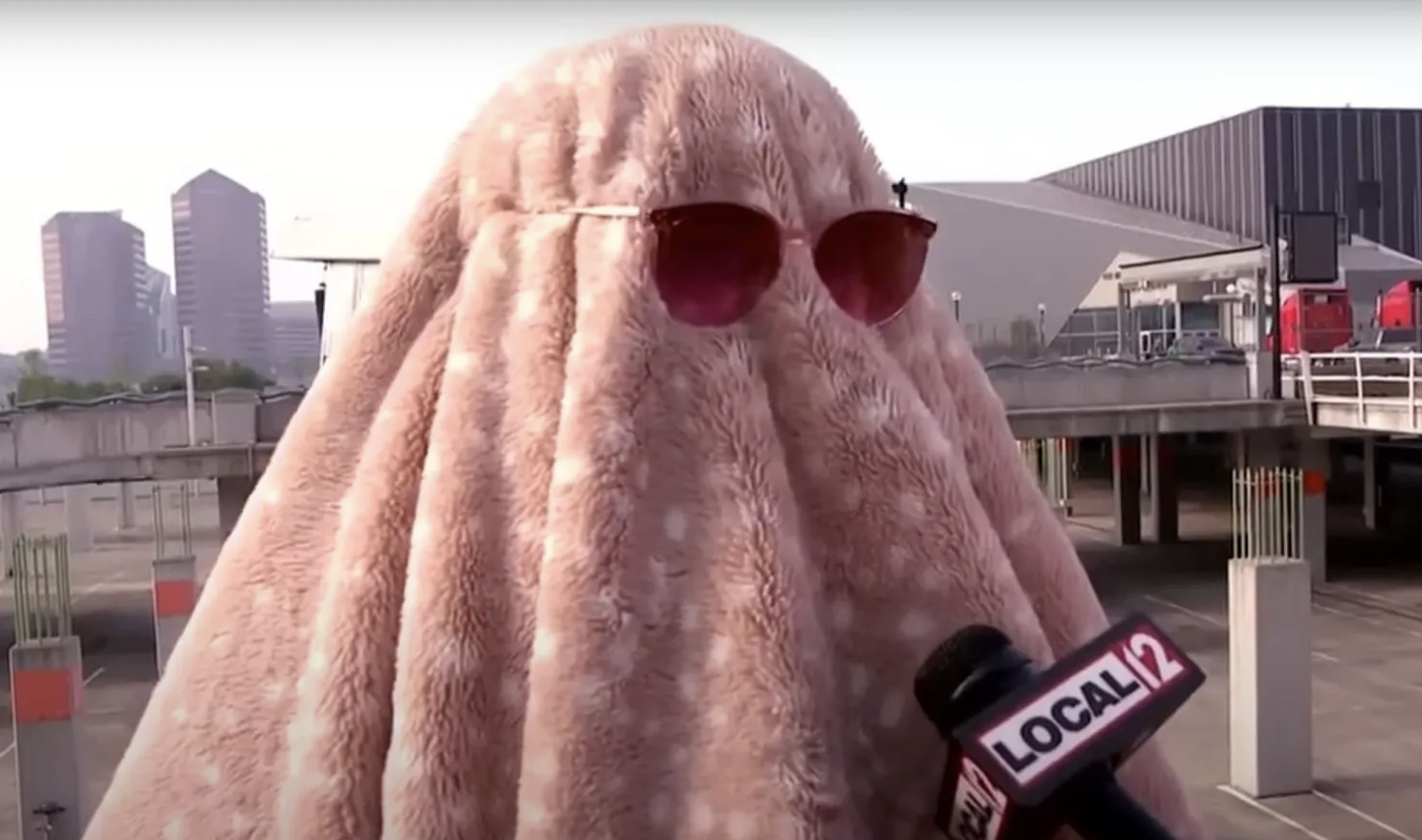 Person in a humorous blanket disguise with sunglasses giving an interview