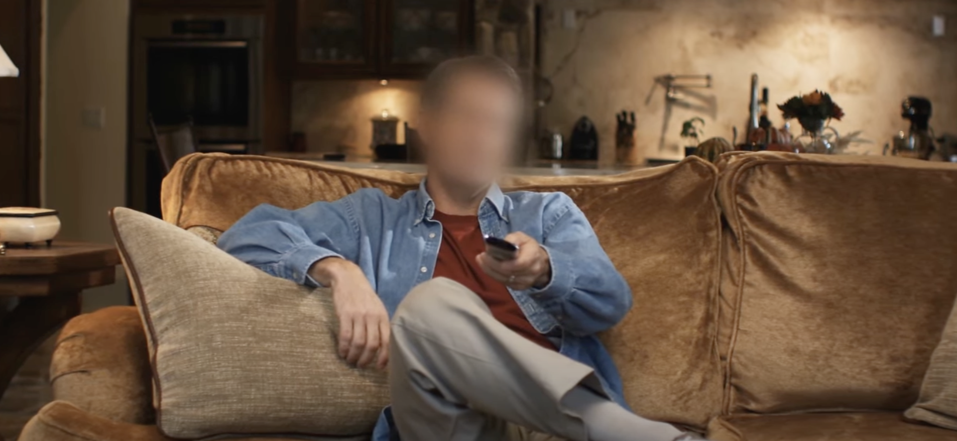 Person relaxing on a sofa holding a remote control with blurred face for privacy