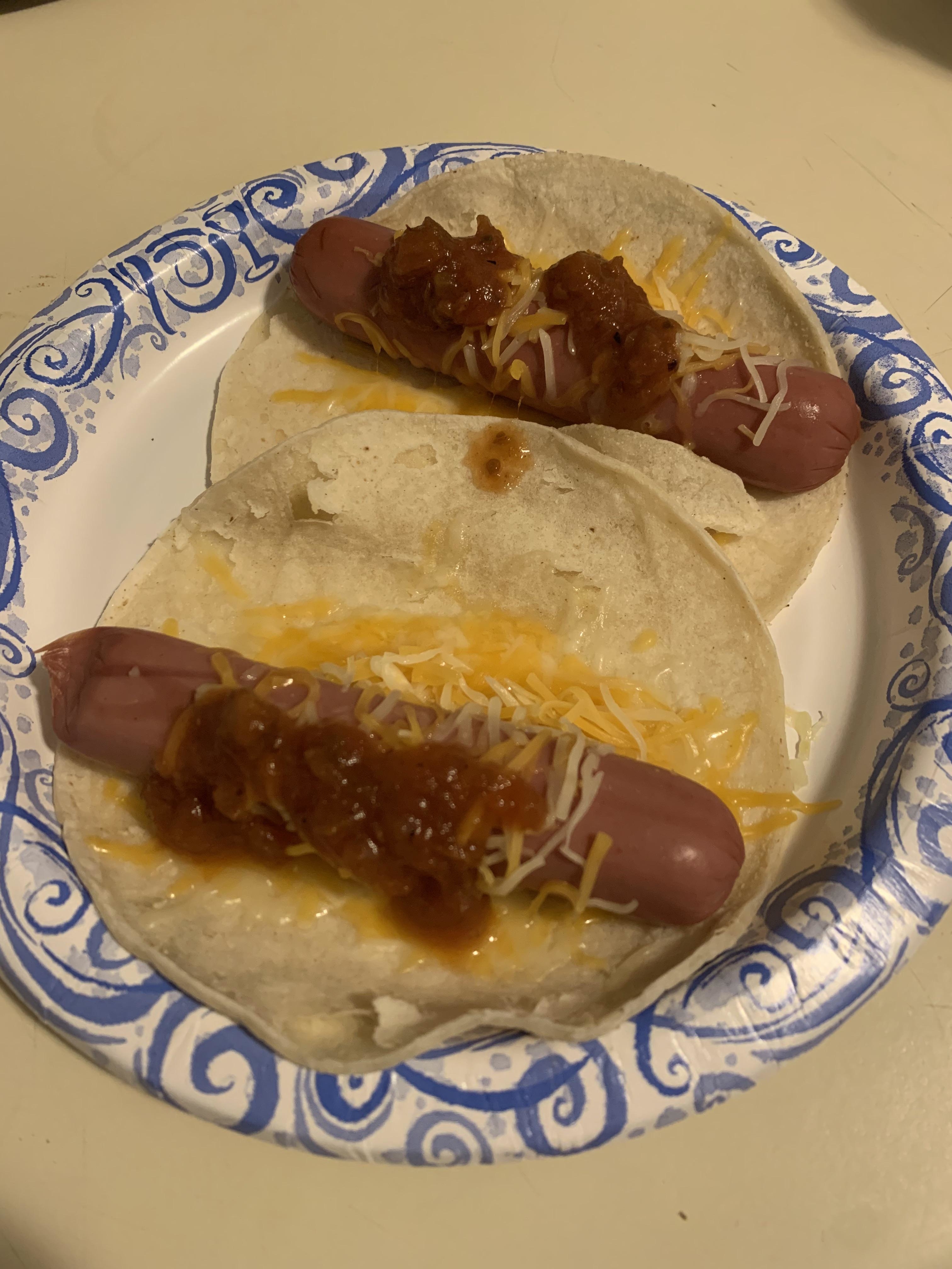 Two hot dogs with cheese and salsa on open tortillas on a plate