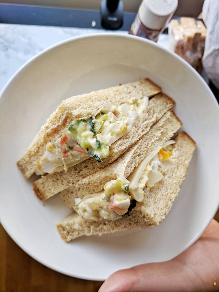 Egg salad sandwich with visible chunks of egg and vegetables on whole grain bread, served on a white plate