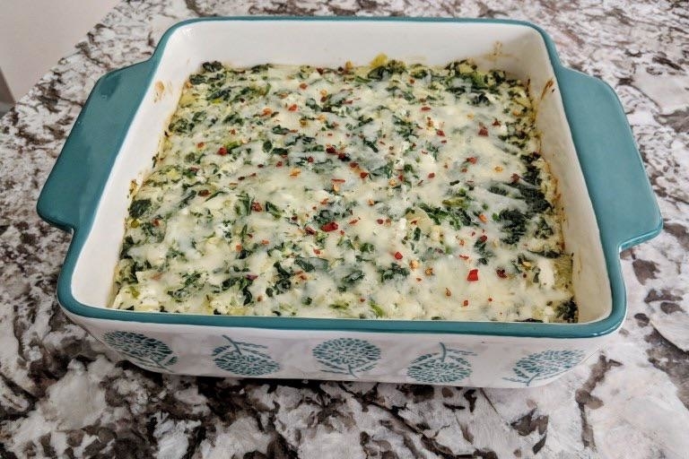 Baked spinach and cheese casserole in a square dish on a marble countertop