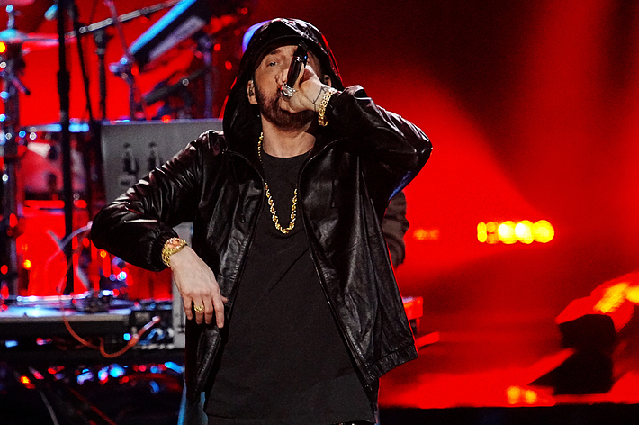 Eminem performs on stage, wearing a leather jacket and holding a microphone