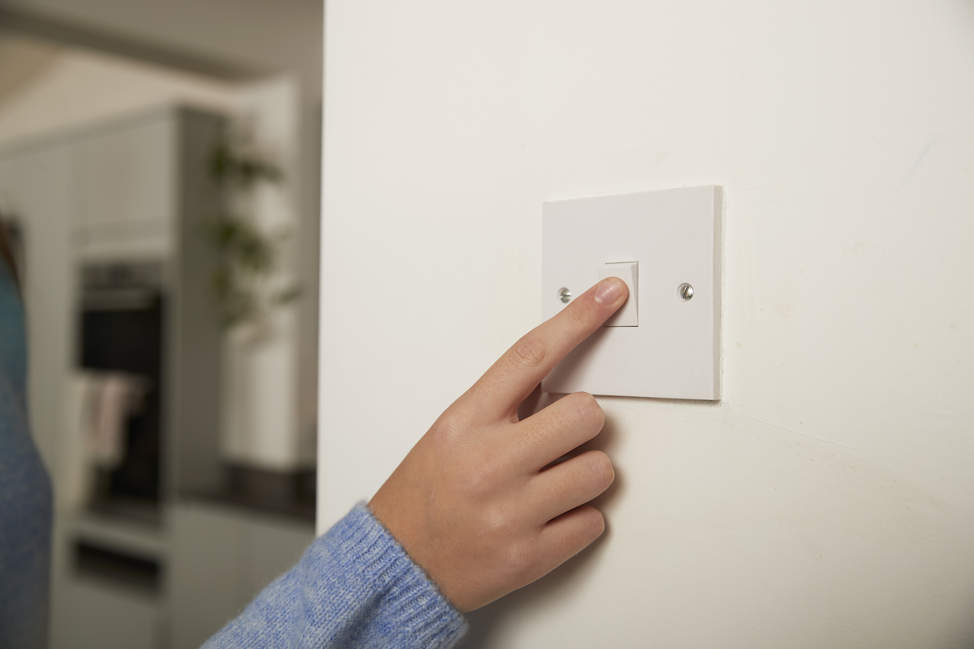 Person&#x27;s finger pressing a light switch on a wall