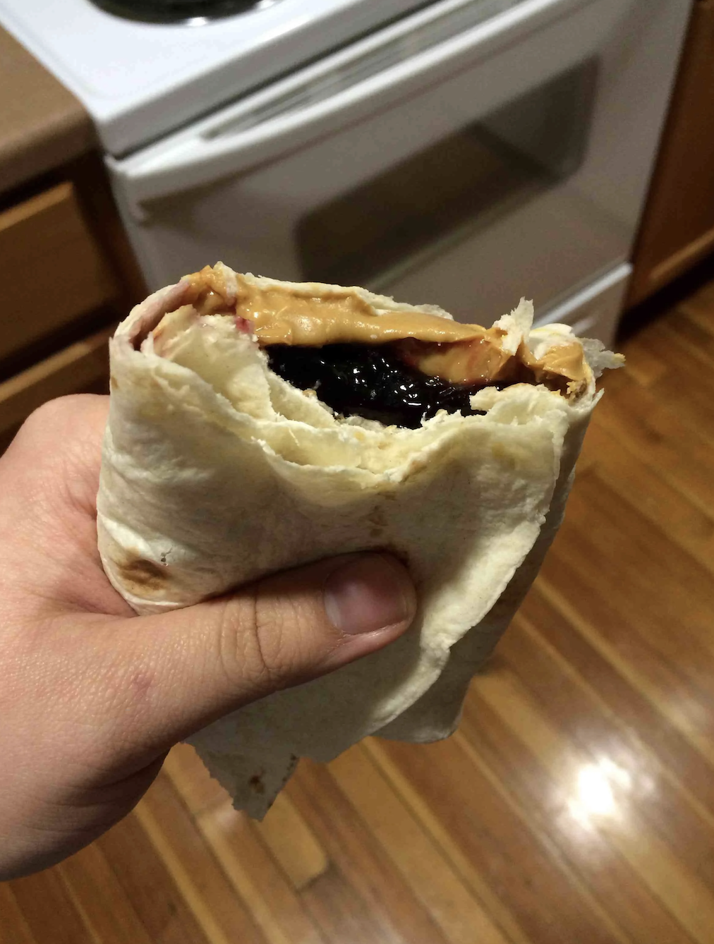 Person holding a half-eaten peanut butter and jelly sandwich wrapped in a tortilla