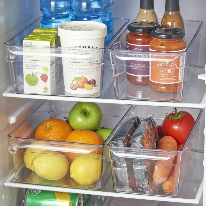 Open refrigerator with an assortment of food items including fruits, vegetables, sauces, and dairy products organized using clear fridge organizer bins