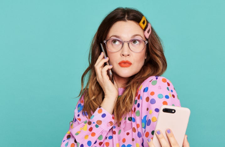 Drew Barrymore wearing the blue light blocking glasses, a polka dot top, and hair clips, holding a phone looking surprised