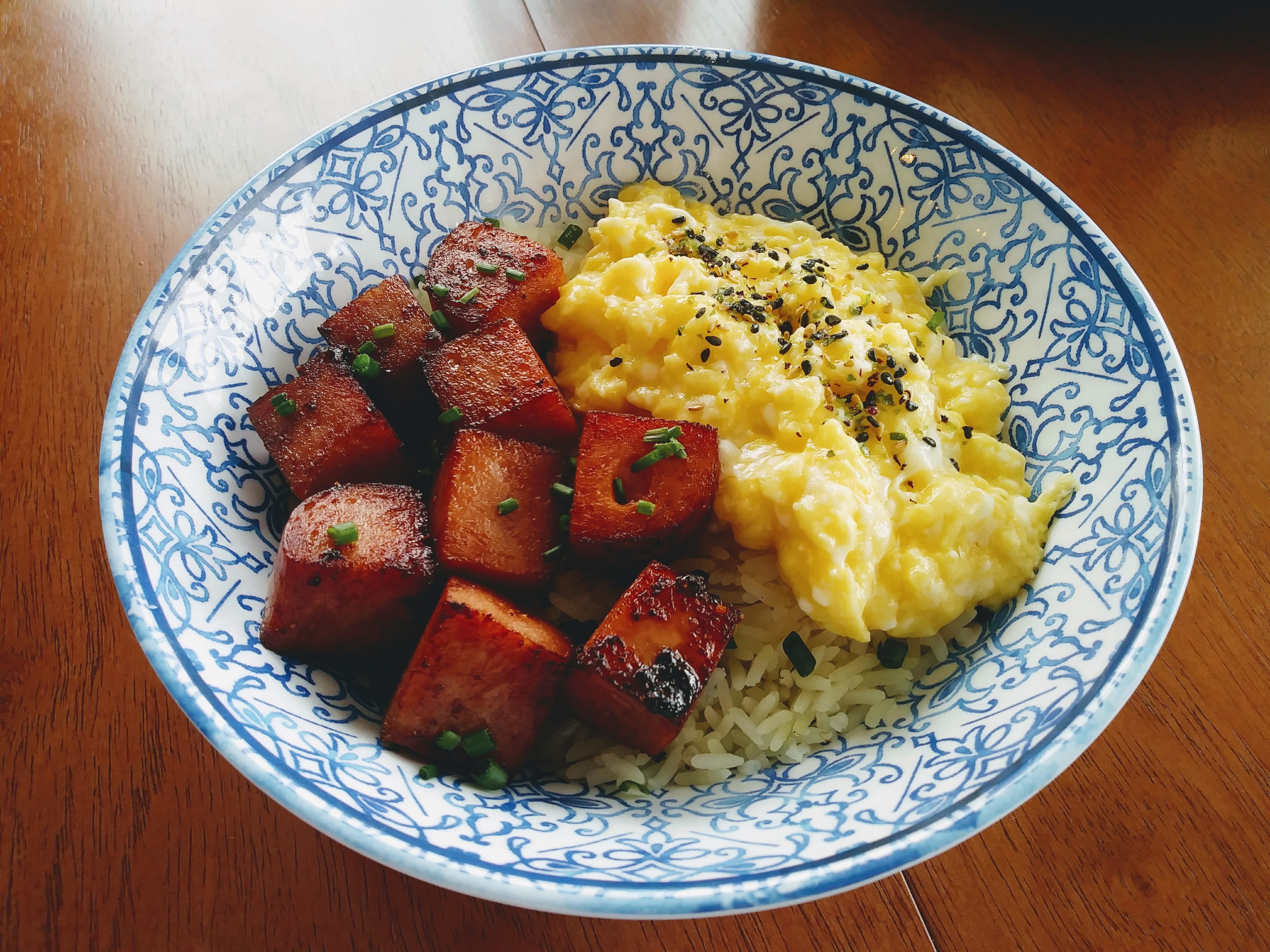 A bowl of rice topped with scrambled eggs and diced ham, garnished with herbs and black pepper