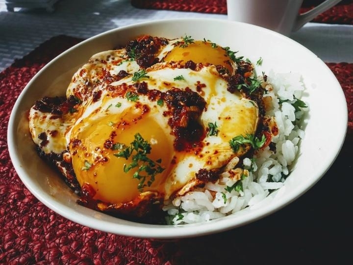 A bowl of rice topped with three fried eggs and chili sauce