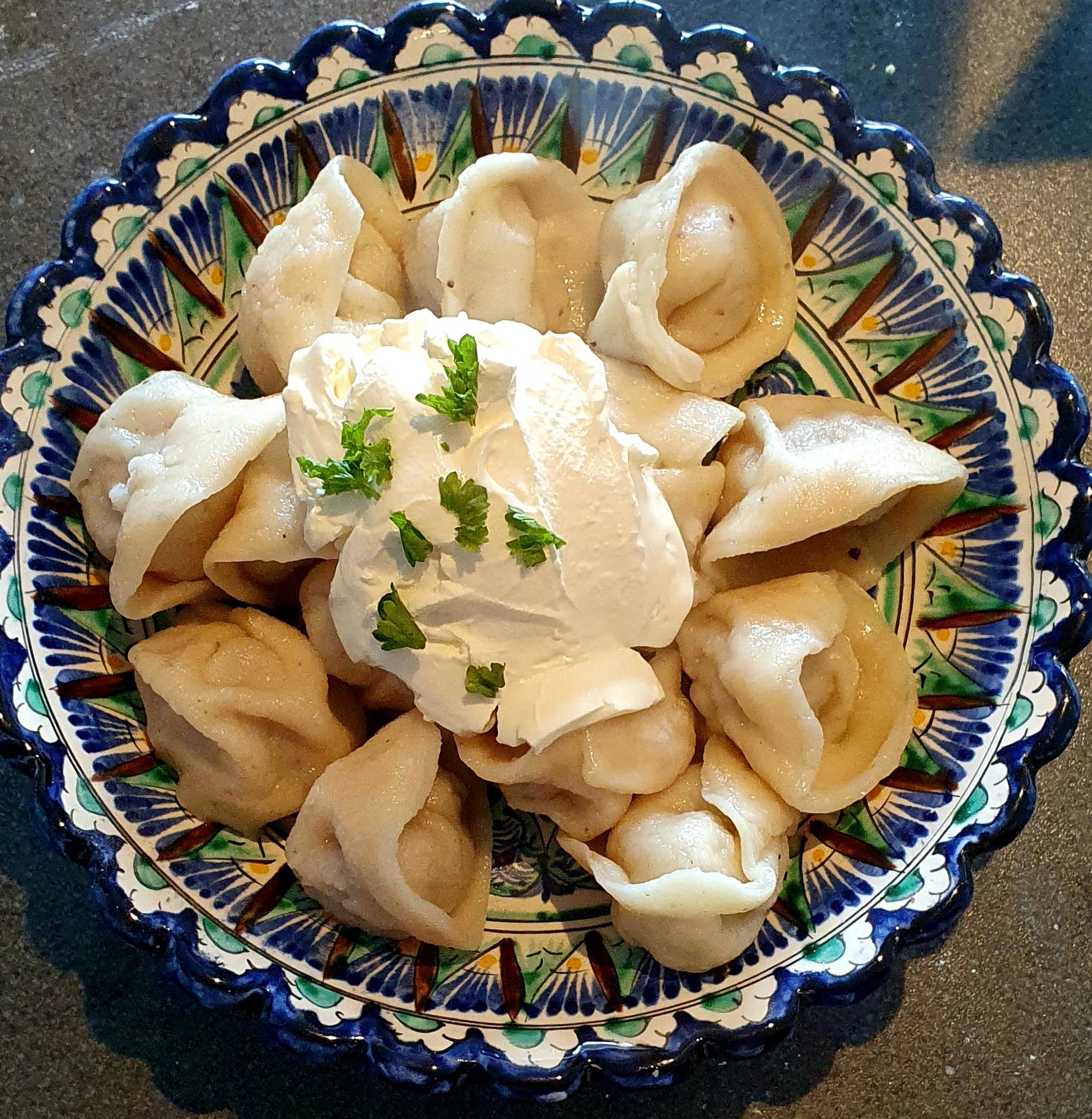 A plate of dumplings topped with sour cream and garnished with herbs